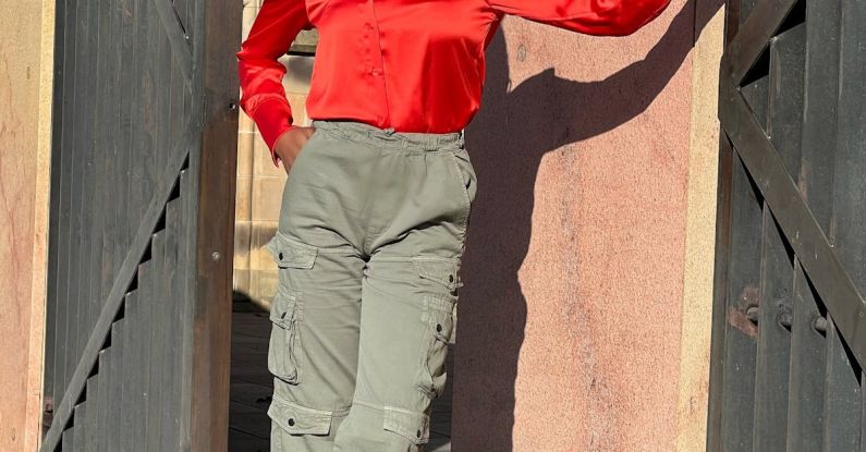 Color Coordinating - A woman in red shirt and green pants standing by a wall