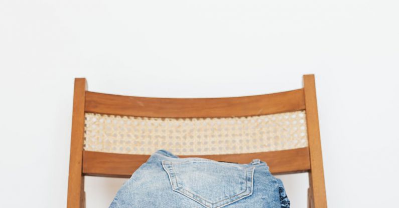 Vintage Jeans - Stack of blue jeans of different shades on modern wooden chair against white wall